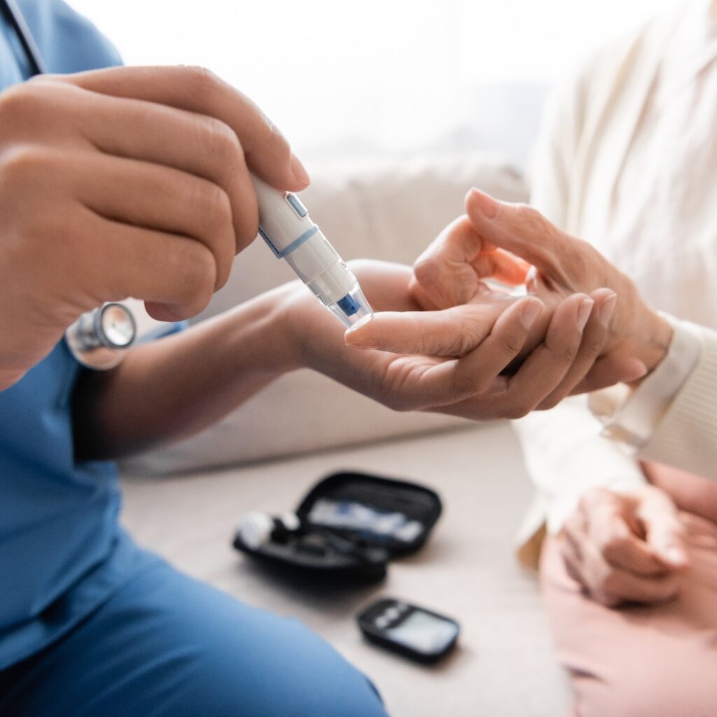 Ausschnitt einer multirassischen Krankenschwester, die einer älteren Frau mit einem Lanzettenstift eine Blutprobe entnimmt.