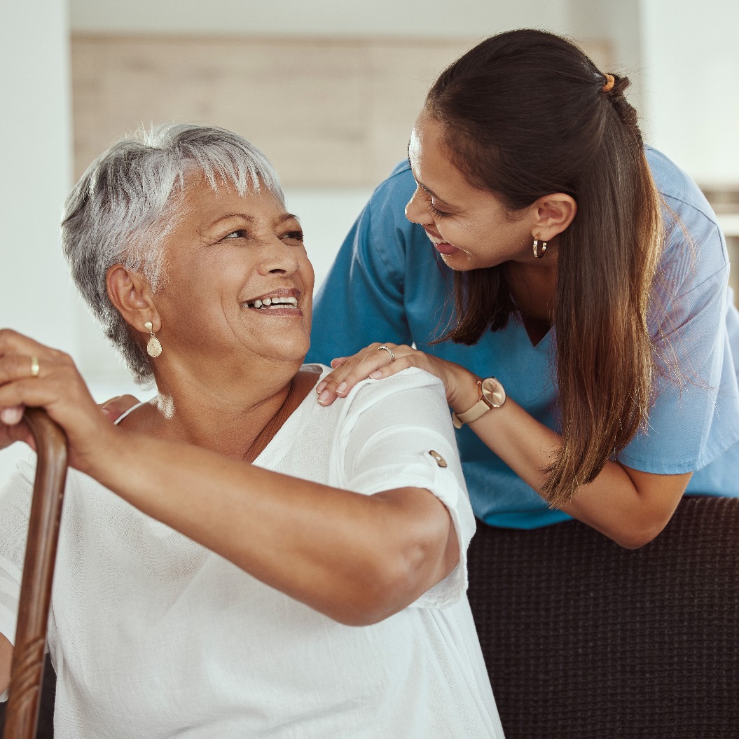 Glückliche, entspannte und ältere Frau mit Pflegerin lächelt, während sie auf einem Wohnzimmersofa in einem Pflegeheim sitzt. Unterstützung, Hilfe und professionelle Krankenschwester oder Pflegekraft, die einer älteren Dame oder einem Patienten hilft