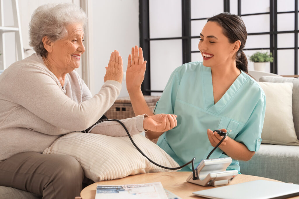 Laechelnde Pflegerin gibt aelterer Frau bei der Blutdruckmessung ein High Five