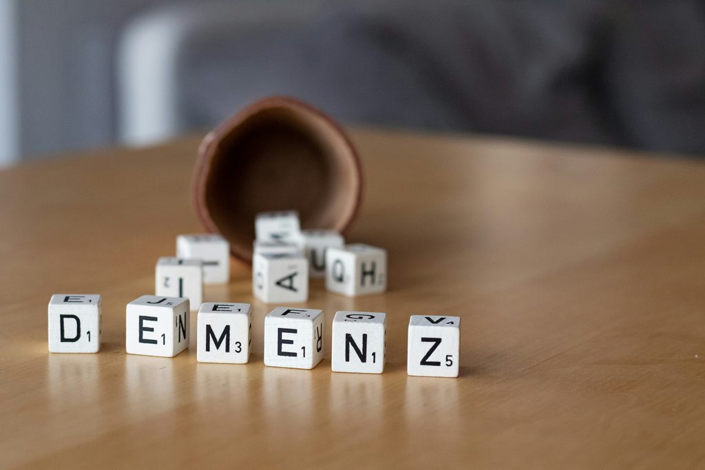 Buchstabenwuerfel bilden das Wort Demenz auf einem Holztisch vor Blumentopf
