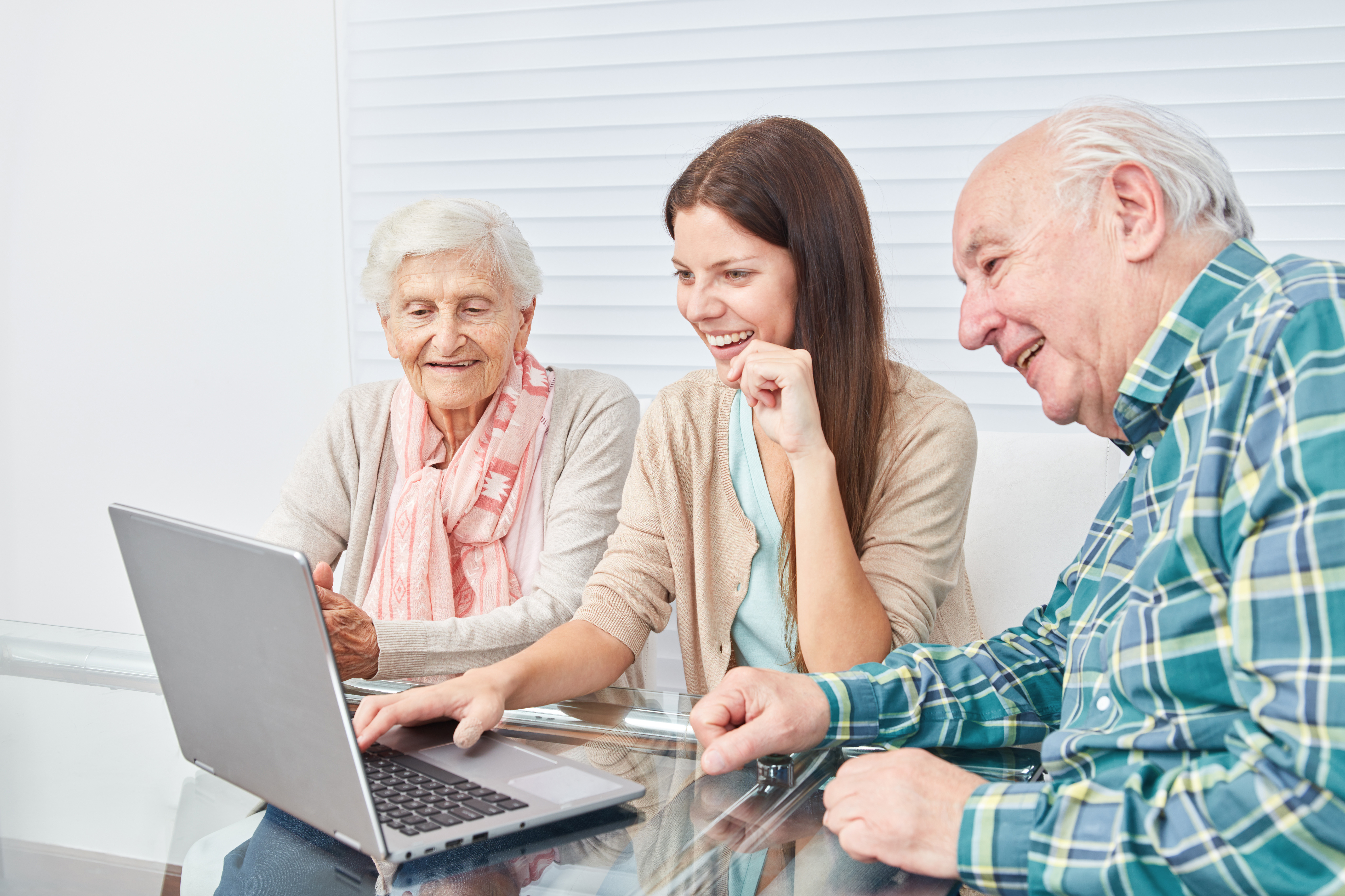 Junge Frau und zwei laechelnde Senioren schauen gemeinsam auf einen Laptop